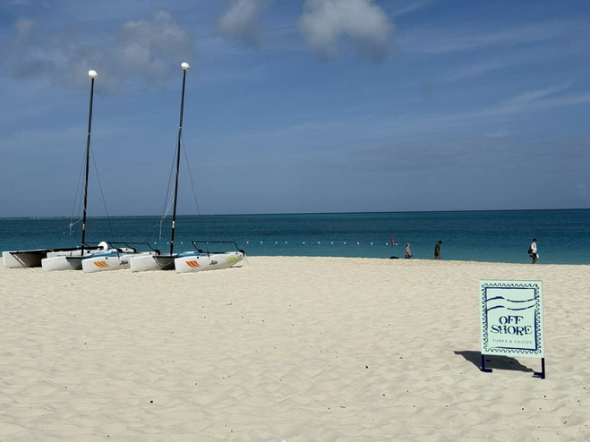 Windsurfing equipment in front of a Restaurant sign with the beach in the background
