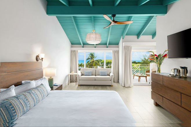 Restful resort room with bedroom furniture and seating area with big windows that overlook island vegetation and the sea