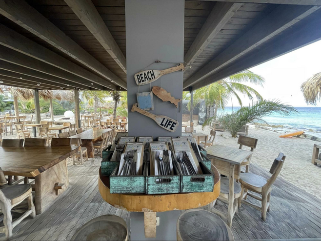 Beachfront Bar overlooking the ocean with palm trees and tables in the background and beach signs in the foreground