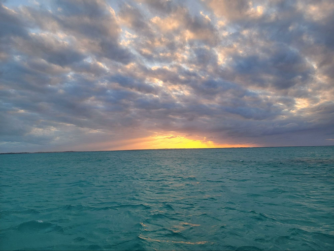 dazzling orange Sunset over deep turquoise water and cloudy sky