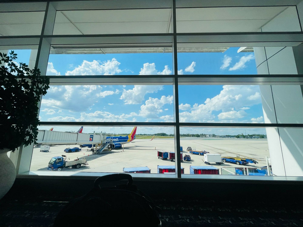 View through window of an airport gate, showing luggage carts, a jetway and a Southwest Airlines airplane.