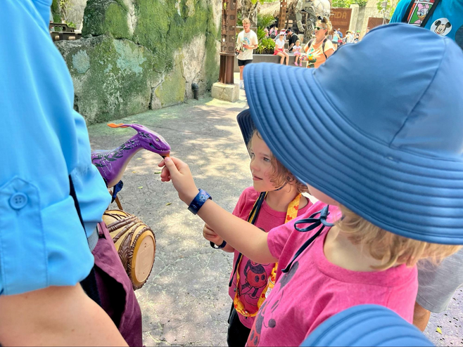 Two children interact with a small banshee animal held by a Disney cast member.