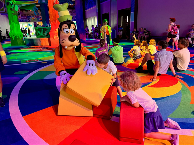 Goofy builds a fort with colorful large building blocks, accompanied by two children.