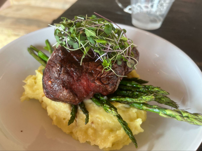 Dinner plate with micro-green-topped grilled steak set on top of asparagus and mashed potatoes.
