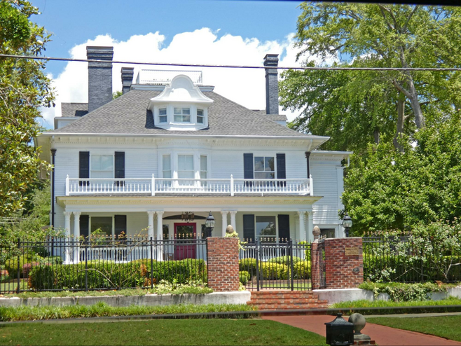 Southern style two story frame home of the 1900s with brick columns at wrought iron gate, widow's walk and attic bay window.