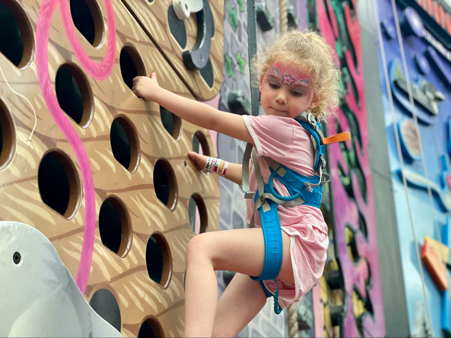 Girl looks down as she climbs an indoor climbing wall at Mall of America
