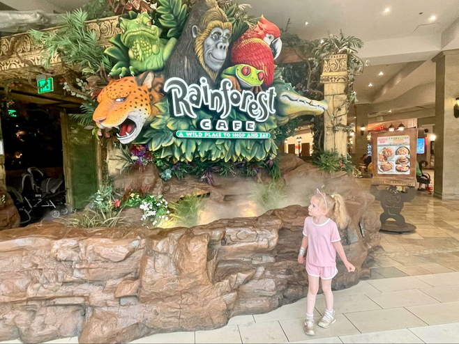 Girl stands in front of a sign for the Rainforest Cafe restaurant