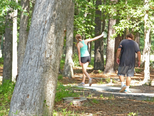 A couple playing disk golf amid trees.