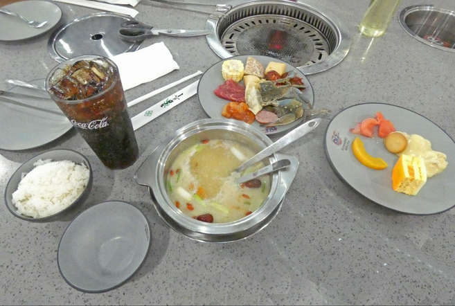 Several plates of food, a glass of coke, and hot pot and BBQ cooker