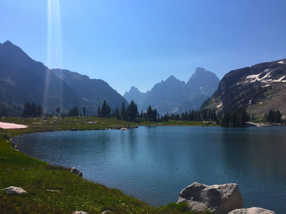 Pretty alpine lake in foreground with craggy mountain peaks in background.