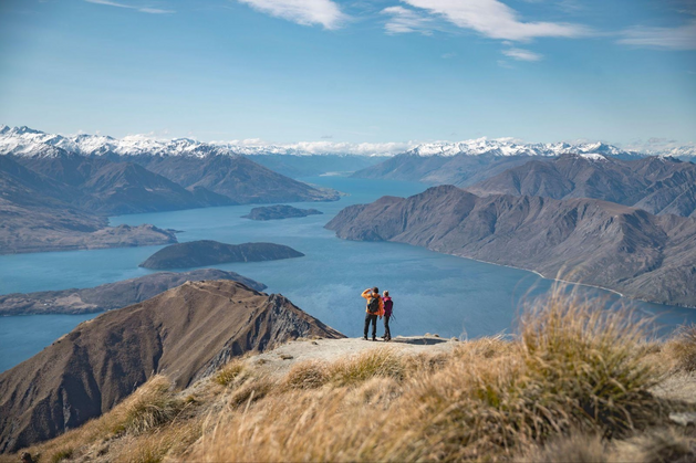 Hikers on mountain top looking out over large lake and surrounding mountains.