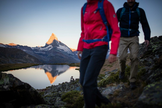 Hikers walking past small lake reflecting the matterhorn.