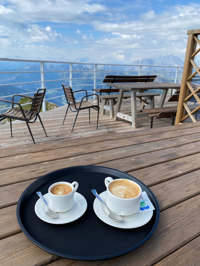 2 coffees on tray on table on platform overlooking surrounding mountains.