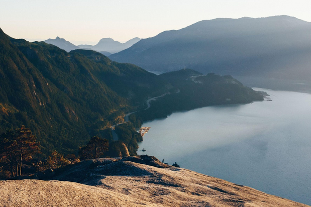 Looking from a mountain top over an ocean inlet and surrounding mounding mountains.