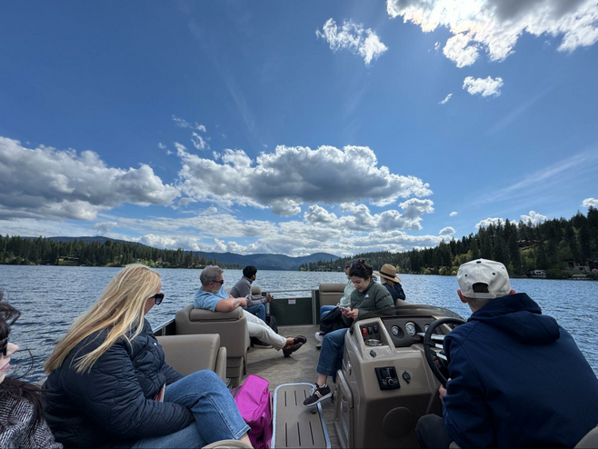 View of Hayden Lake from a boat with forests and mountains in the distance. The sky is blue with white clouds.