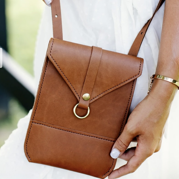 Closeup of a chestnut colored leather crossbody bag with brushed gold accents