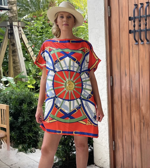 Woman wearing a hat and a mini silk tunic with a bold primary colored print.