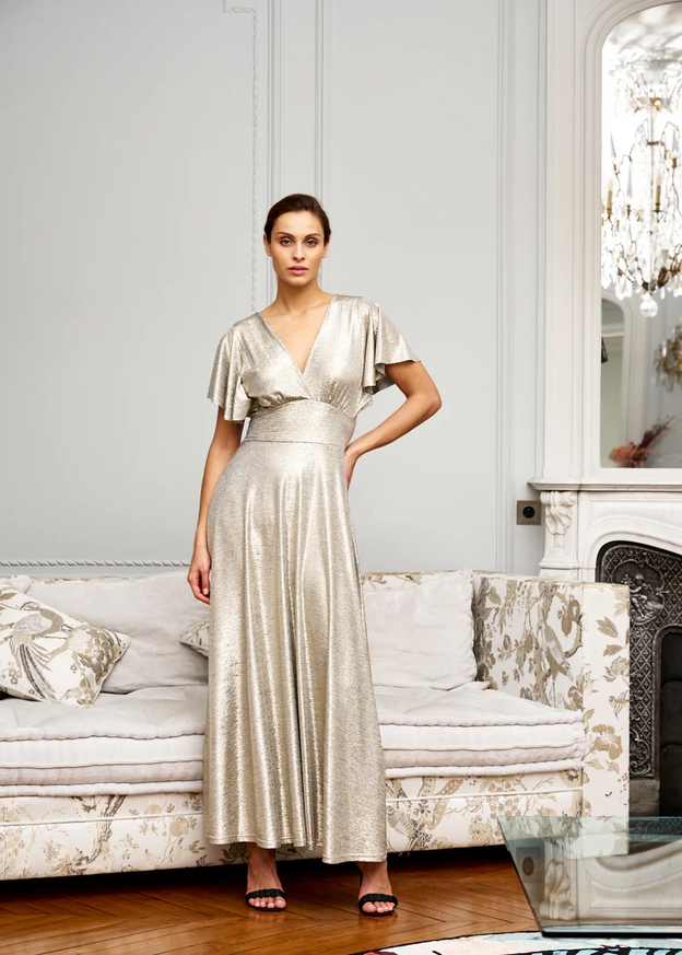 Woman wearing a long gold dress standing in front of an elegant sofa
