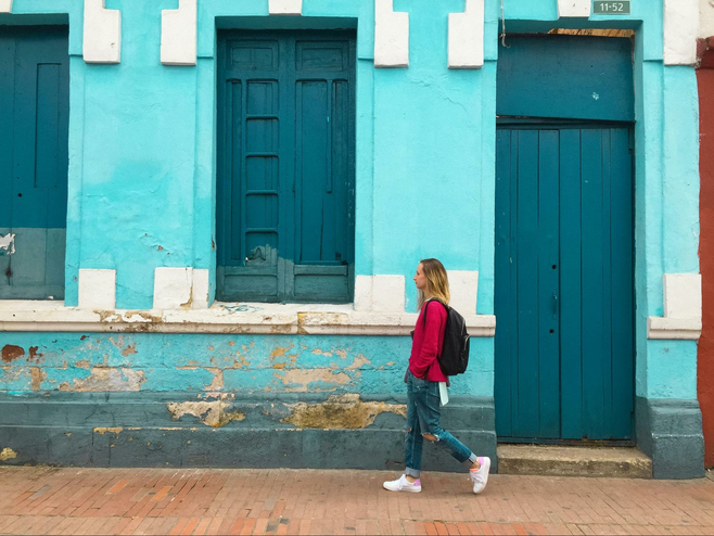 Woman wearing a backpack and walking pastg a blue building with blue painted doors