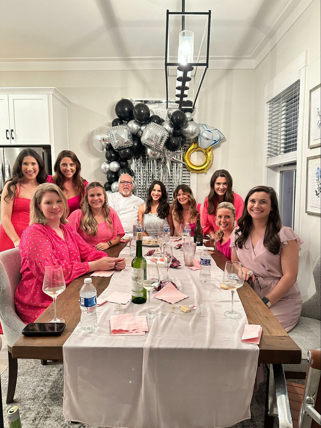 Engagement party of women all dressed in pink except for the bride-to-be in silver and the chef in his chef coat.