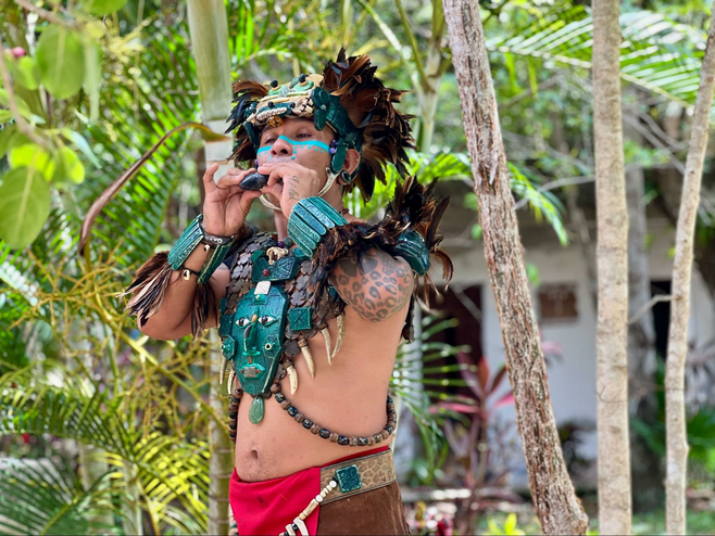 Man in ceremonial Mayan outfit playing a flute