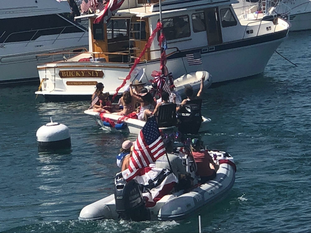 Two dinghies in the water in front of a yacht, all decorated for July 4th.