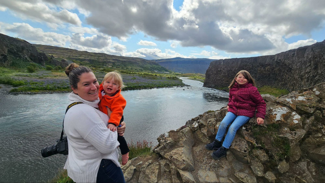 Woman holding a baby and a girl posing along a river in Iceland.