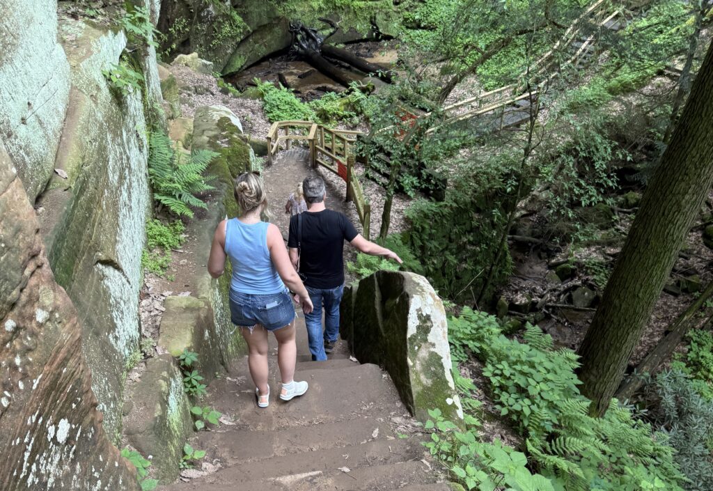 A women and man from behind as they are walking down a stone staircase with greenery around.