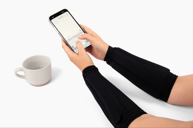 Two arms with compression sleeves on the forearms, holding a smart phone with a coffee cup to the side.