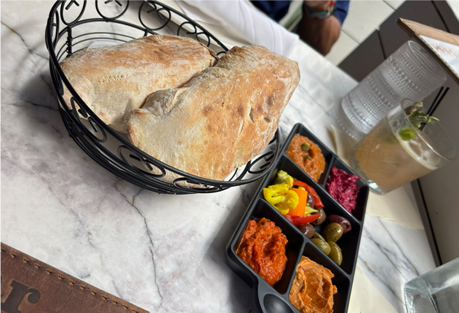 A basket with pita bread next to a tray of four colorfuldips and vegetables.
