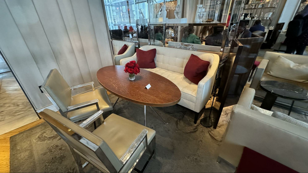 White sofa with red pillows and two armchairs next to an oval table with roses.