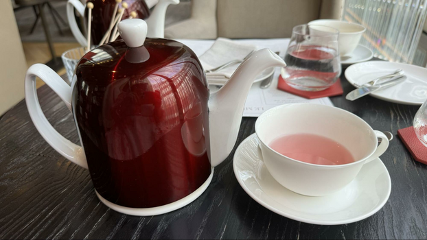 Red teapot and tea cup and saucer filled with pink tea on table.