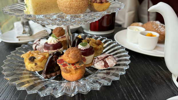 Ten pastries on a clear plate next to a tea pot.