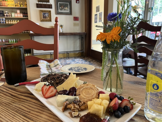 Cheese platter with cookies, fruit and nuts on a table with vase of flowers