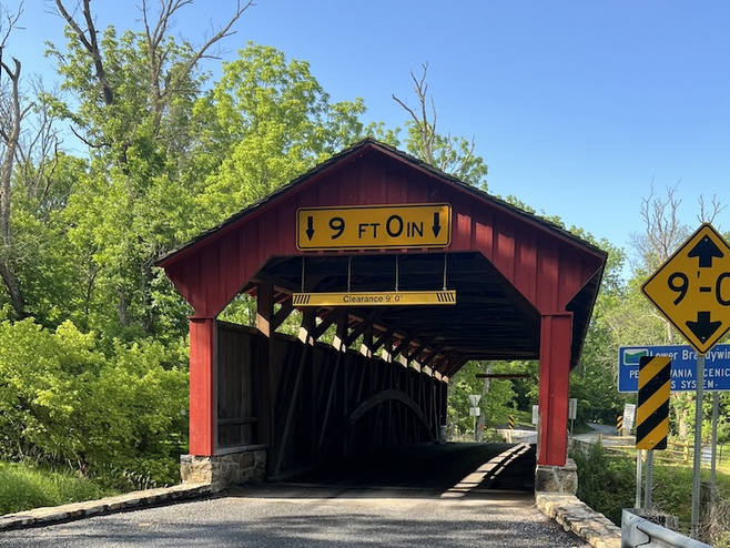Red wood covered bridge surrounded by green trees.