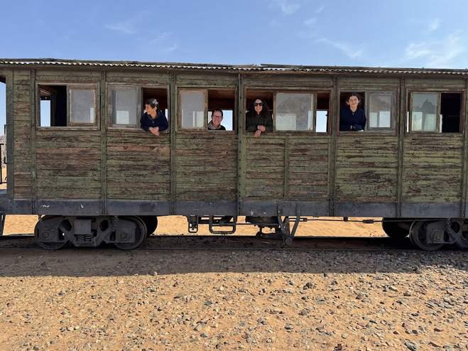 Mom, Dad, son, and daughter on an old train in Jordan. The train has peeling green paint over wood.