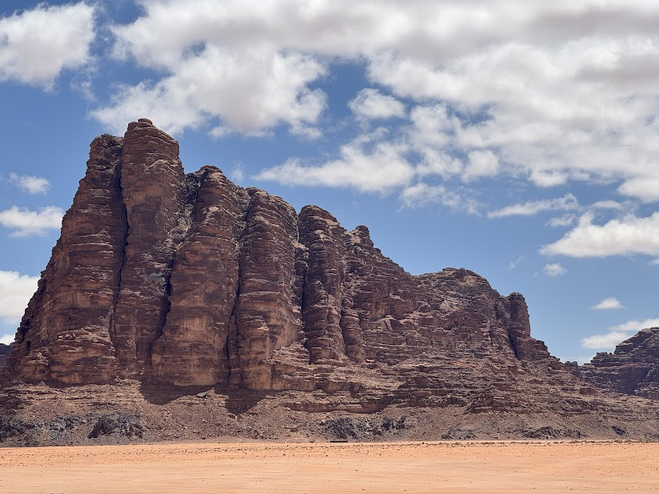 Four red columns in the desert against a blue sky with white clouds.