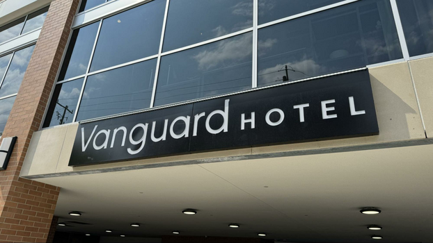 Black plaque with Vanguard Hotel etched into it on the side of a building with tall windows.