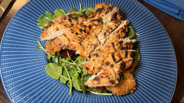 Grilled chicken strips on top of green spinach leaves on a circular blue plate.