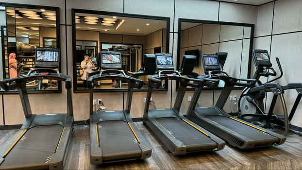 Four treadmills and an elliptical against wall mirrors inside of a gym.