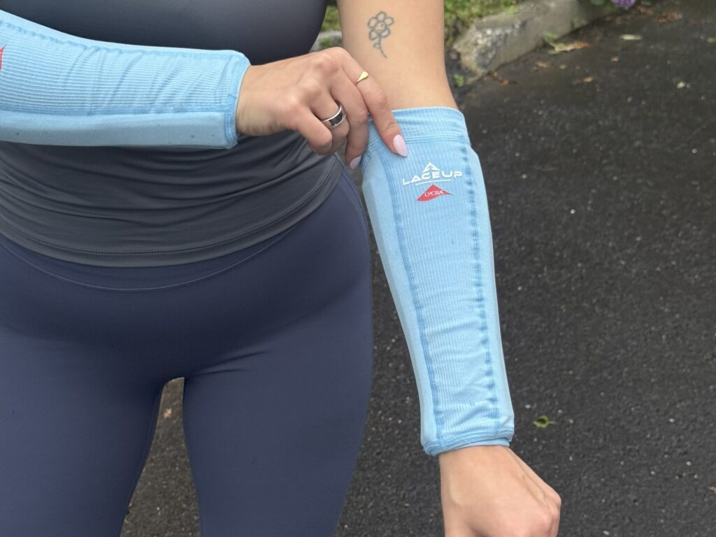 View of a woman in black exercise clothes with light blue weighted compressions sleeves on her forearms, pulling one sleeve up with the other hand.
