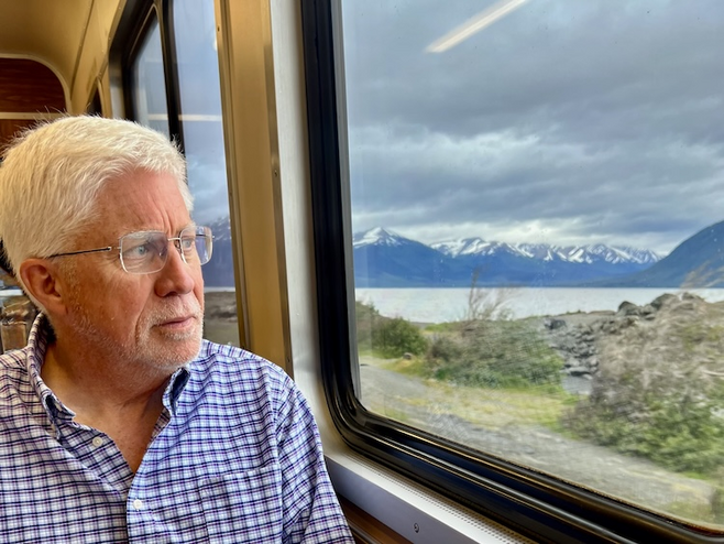 Man gaze out train windows at snow topped mountain and lakes