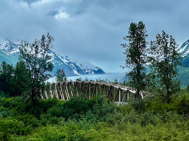 Glacier view surrounded by mountains and bridge trestle in the foreground.