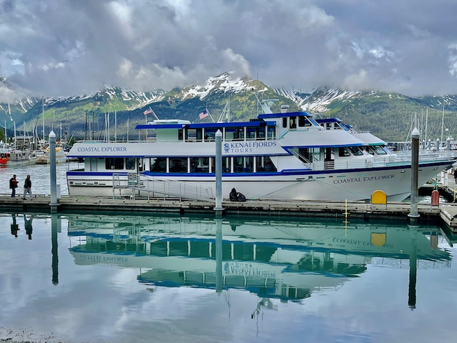 Cruise boat in harbor preparing to board passengers framed by mountains.