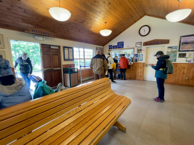Depot in Seward with people waiting to buy a ticket and wooden bench in foreground.