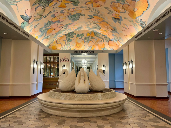 A fountain with three swans and a colorful ceiling mural of orange flowers. 