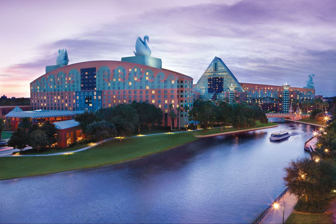 An ornate coral-and-turquoise hotel is pictured at sunset, topped by enormous Swan statues on its rooftop.