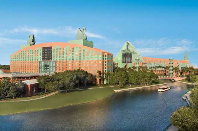 An ornate coral-and-turquoise hotel is pictured in daylight, topped by enormous Swan statues on its rooftop. A boat is traveling in the waterway in front of the hotel.