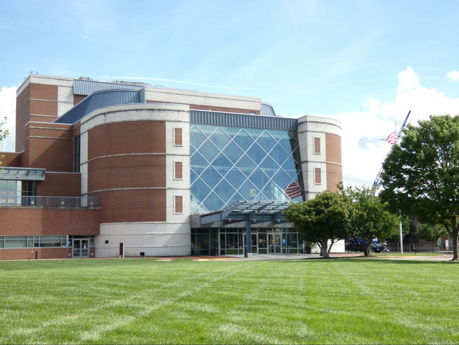 Red brick building with glass front and metal awning over entrance on grassy lawn.