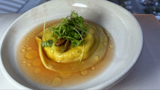 White bowl filled with extra virgin olive oil and a circular stuffed goat cheese ravioli topped with green fennel.